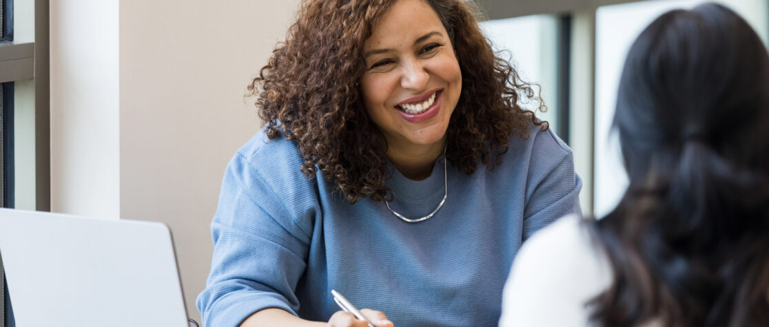 The mature adult female business owner smiles encouragingly at an unrecognizable female job applicant.